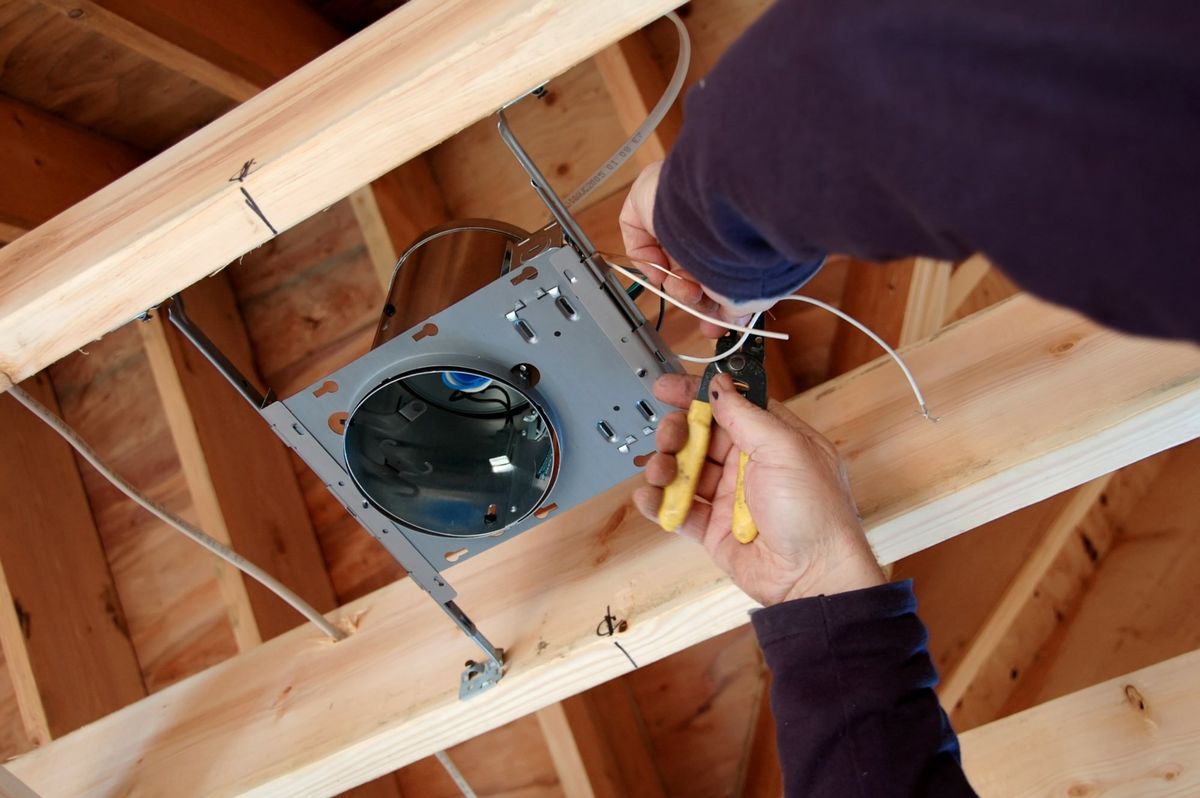Electrician wiring a new-construction recessed light housing mounted between open ceiling joists