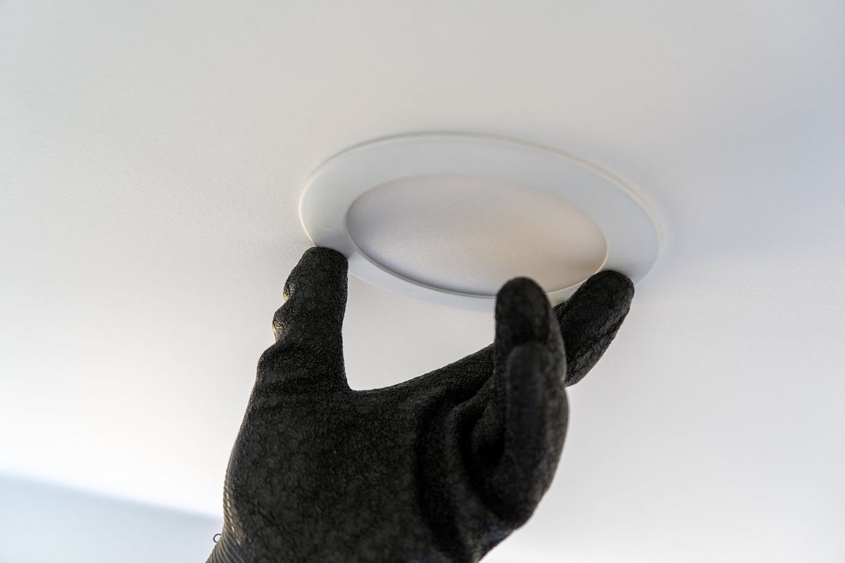 Gloved hand pressing a slim LED recessed light trim into a white ceiling