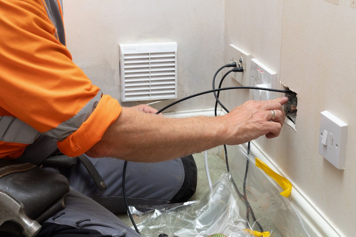 Electrician kneeling at a wall, feeding cable into an opened box beside the outlets