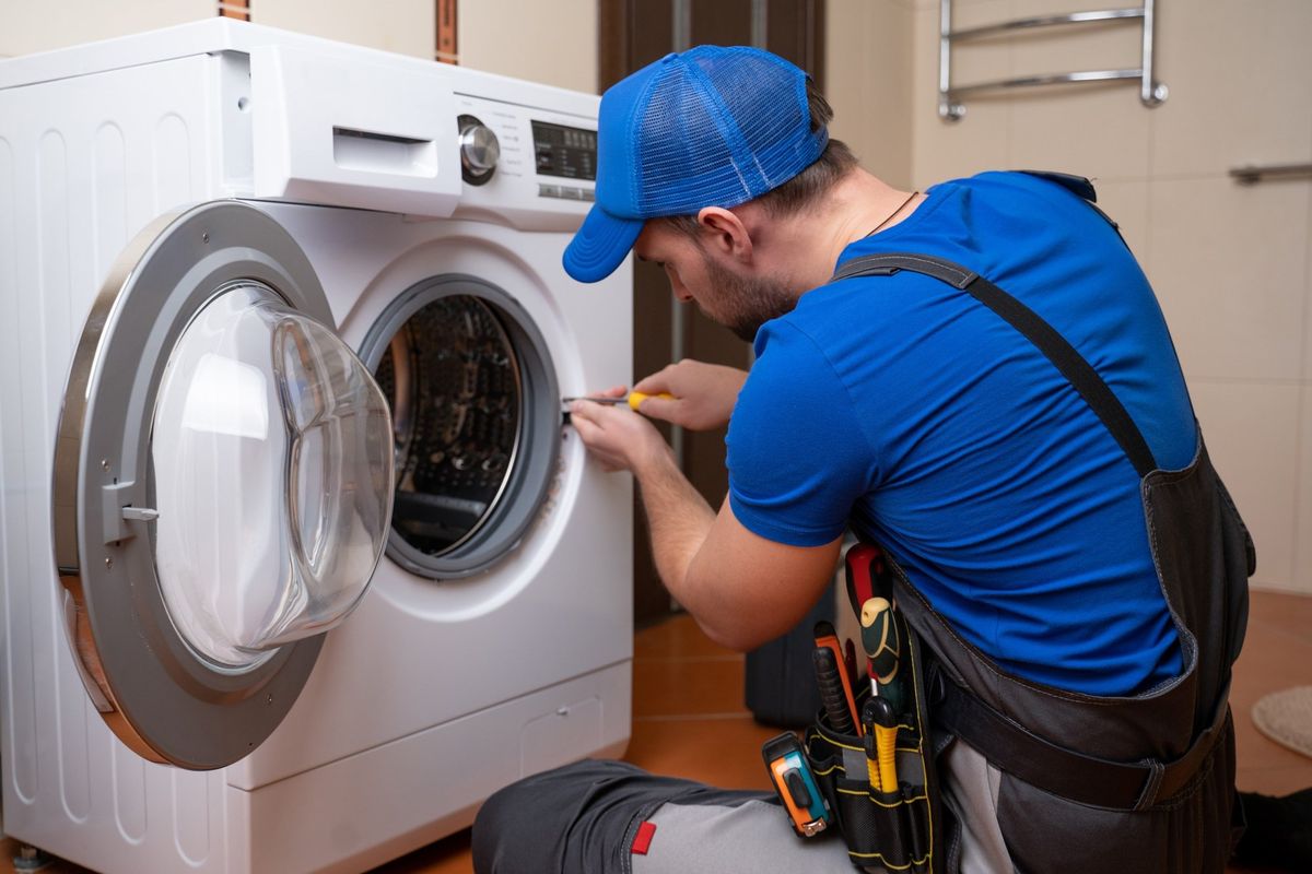 Technician in a blue cap working on a front-load washing machine